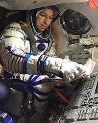 Astronaut in a spacesuit works with controls inside a spacecraft simulator.